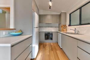 a kitchen with white cabinets and a wooden floor at Lockhart Leafy Cottage - walk to Mollymook Beach in Mollymook +3 photos