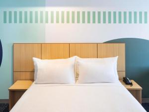 una cama con almohadas blancas y un cabecero de madera en ibis Styles Sydney Central, en Sídney