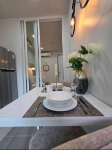 une table blanche avec une assiette et un vase de fleurs dans l'établissement The Modern central Phuket base condo by luxStays, à Ban Rangeng