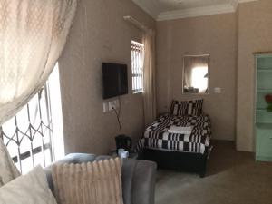 ein Schlafzimmer mit einem Bett, einer Couch und einem Fernseher in der Unterkunft Long Avenue Guest House in Johannesburg