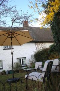 a group of chairs and an umbrella in front of a house at Snowdrop Cottage in Jacobstowe +21 photos