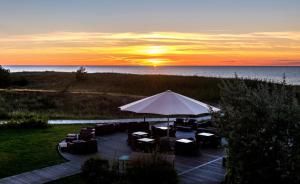 een terras met stoelen en een parasol met de zonsondergang bij Strandhotel Dünenmeer - Adults only in Dierhagen