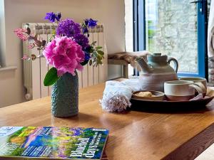 a table with a vase of purple flowers and a book at The Owlery At Aysgarth in Aysgarth