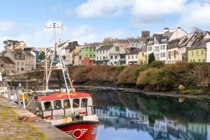 Un bateau rouge est amarré sur une rivière bordée de maisons. dans l'établissement Cottage 494 - Roundstone, à Roundstone