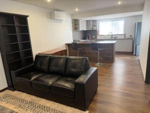 a living room with a leather couch and a kitchen at Self-Contained Studio in Loganholme