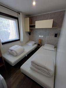 two beds in a small room with a window at Mobil home 6 personnes 3 chambres in Pont-Aven