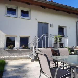 Un patio con una mesa de vidrio y sillas frente a un edificio. en Ferienwohnung An der Kapf, en Münsingen