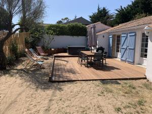 eine Holzterrasse mit einem Tisch, Stühlen und einem Sonnenschirm in der Unterkunft Maison de vacances , idéale pour famille avec accès plage et spa in Barbâtre