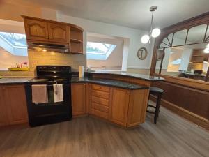 uma cozinha com armários de madeira e um fogão preto em Entire floor in a Spacious bungalow ensuite close to beach and train em Pincourt mais 13 fotografias