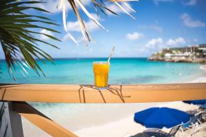 a glass of orange juice sitting on a railing overlooking the ocean at Royal Islander Club Resort La Terrasse in Lowlands