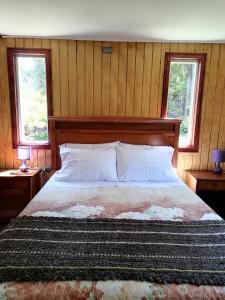 Un dormitorio con una cama grande con dos ventanas. en Cabañas CyG - Chaitén, en Chaitén