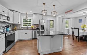 une cuisine avec des armoires blanches et un réfrigérateur en acier inoxydable dans l'établissement Stylish 4BR Getaway with Game Room, Grills & Cozy Outdoor Fire-Pit, à Cary