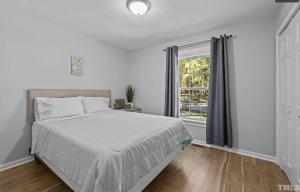 une chambre blanche avec un lit et une fenêtre dans l'établissement Stylish 4BR Getaway with Game Room, Grills & Cozy Outdoor Fire-Pit, à Cary