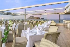 a restaurant with white tables and chairs and the ocean at Porto Platanias Beach Resort & Spa in Plataniás
