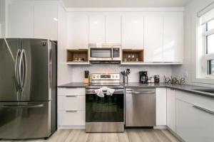 a kitchen with stainless steel appliances and white cabinets at 5BDRM Chic Modern Home-Hot Tub-King Bed-AC-Garage in Edmonton