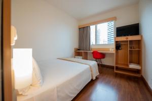 Una habitación de hotel con una cama blanca y una silla roja. en Ibis Florianopolis, en Florianópolis