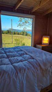 a bed in a room with a large window at CABAÑA MIRADOR in Quemchi