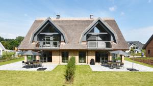a house with a large roof with tables and umbrellas at Exklusive Reetdach-Villa Ostseefrische in Lobbe