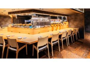 une longue table en bois avec des chaises et une cuisine dans l'établissement Smile Hotel Premium Kanazawa Higashiguchi Ekimae - Vacation STAY 73592v, à Housai