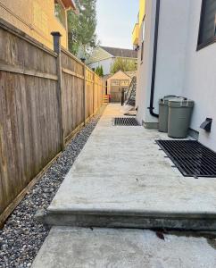 a wooden fence next to a sidewalk with two trash cans at Excellent Place to Stay in Coquitlam