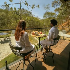 un homme et une femme assis à une table sur un pont dans l'établissement Chalé com banheira, piscina e cachoeira privativa, à Taubaté