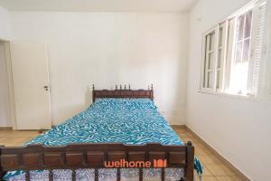 ein Schlafzimmer mit einem Bett mit blauer Bettdecke und einem Fenster in der Unterkunft Casa no Centro de Peruibe a 750m da Praia in Peruíbe