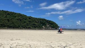 two people sitting under an umbrella on the beach at Casa térrea moderna em condomínio in Bertioga