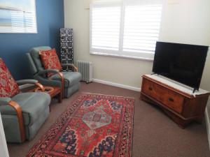 ein Wohnzimmer mit einem TV, einem Sofa und einem Stuhl in der Unterkunft Lakes Entrance Waterfront Cottages with King Beds in Lakes Entrance