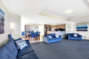 a living room with two blue couches and a kitchen at Coast View - 39b Hargreaves - Family - Beach - No Linen Included in Middleton
