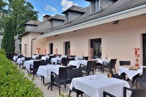 um restaurante com mesas e cadeiras brancas em frente a um edifício em Hôtel Restaurant Les Coquelicots, The Originals Relais (Inter-Hotel) em Saint-Pardoux-lʼOrtigier