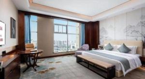 a bedroom with a large bed and a desk and window at Ramada by Wyndham Wuhan Dongxihu in Wuhan