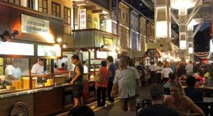 Un grupo de personas de pie alrededor de un patio de comidas en un restaurante. en Royal Hostel Singapore, en Singapur