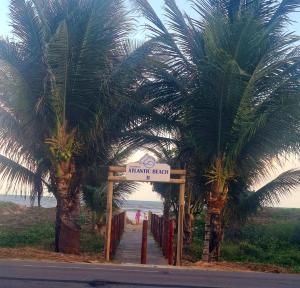 a sign for an entrance to a beach with palm trees at Casa cinza em frente à praia em condominio in Aracaju