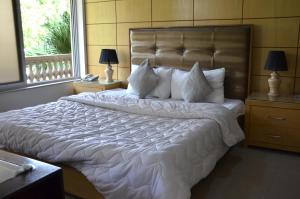 1 dormitorio con 1 cama grande con sábanas y almohadas blancas en Gofas Lodge, en Islamabad