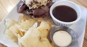 Un plato con un sándwich y patatas fritas y una taza de salsa. en Keuka Lake Motel, en Keuka