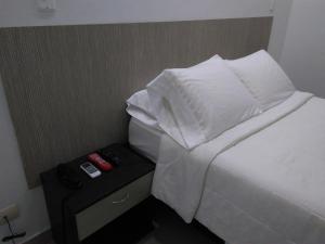 1 cama con sábanas blancas y almohadas encima de una mesita de noche en Hotel Boutique Santorini Class en Sincelejo