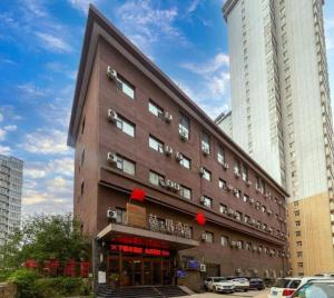 a large brown building with cars parked in front of it at James Joyce Coffetel Xi'an Lingtong The Terracotta Army Huaqingchi University Town Metro Station in Xi'an