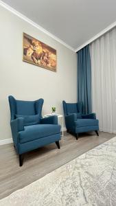 a living room with two blue chairs and a rug at Athletic City, 1-Room Apartments in Taldykolʼ