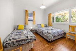 een slaapkamer met twee bedden en twee ramen bij Banksia Cottage - Pet Friendly Waterfront in Callala Bay