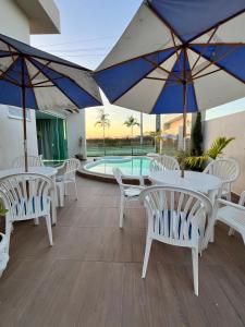 eine Terrasse mit weißen Tischen und Sonnenschirmen und ein Pool in der Unterkunft Casa PWG Cânions - Sua casa de temporada no paraíso in Piranhas
