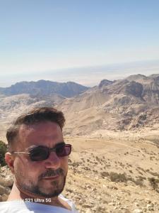 a man wearing sunglasses standing on top of a mountain at aqaba Almahdud in Aqaba