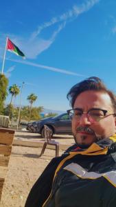 a man wearing glasses sitting on a bench under an umbrella at aqaba Almahdud in Aqaba