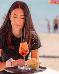 a woman sitting at a table with a drink and a bowl of food at GFH - Hotel Spiaggia D'Oro in Marotta