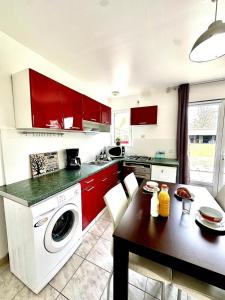 a kitchen with red cabinets and a table with a washer at Les Roses-Plain-pied-St Valery & Le Crotoy à 10min in Noyelles-sur-Mer