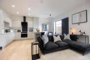 ein Wohnzimmer mit einer schwarzen Couch und einer Küche in der Unterkunft Elliot Oliver - Stunning 4 Bedroom Home with Parking in Cheltenham in Cheltenham