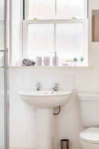 ein weißes Badezimmer mit Waschbecken und Fenster in der Unterkunft Cosy Cottage-Like Apartments Axminster in Axminster