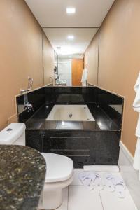 a bathroom with a toilet and a bath tub at Golden Tulip Porto Vitória in Vitória