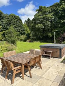 Una mesa de picnic de madera y un banco junto a un jacuzzi. en The Farmhouse at Solsgirth Home Farm, en Dollar