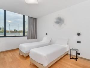 a white room with two beds and a window at B&B HOTEL Alba in Alba