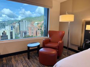 ボゴタにあるヒルトン ボゴタの椅子と大きな窓が備わるホテルルームです。